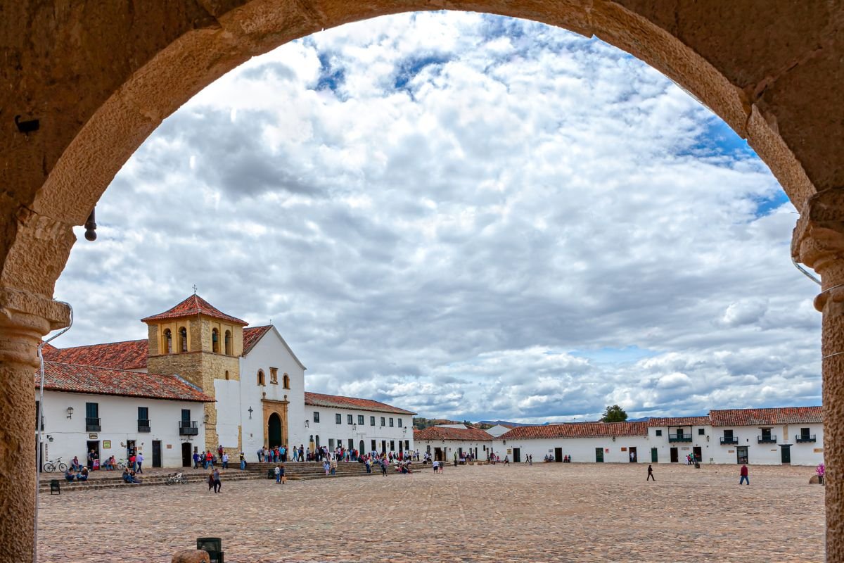 Plaza Mayor of Villa de Leyva and its white church seen through a stone arch